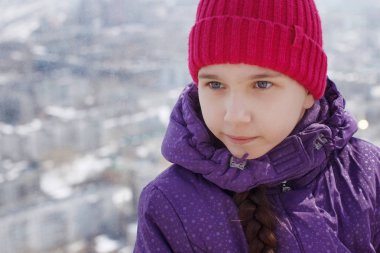Mor şapkalı bir ponpon ile uzun bir örgü ile küçük güzel kız gülümsüyor ve sol görünüyor