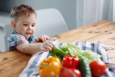 Sevimli küçük sarışın çocuk masada yeşil, sarı ve kırmızı sebze salata yapmak hazırlık yapıyordu