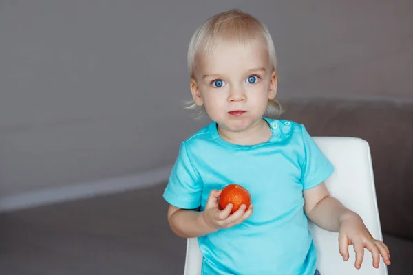 Söt Pojke Med Blont Hår Och Blå Ögon Äter Apelsin — Stockfoto