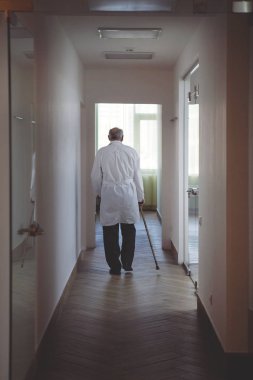 Yaşlı bir doktor bastonla Beyaz paltolu koridor boyunca mesafe içine bırakır