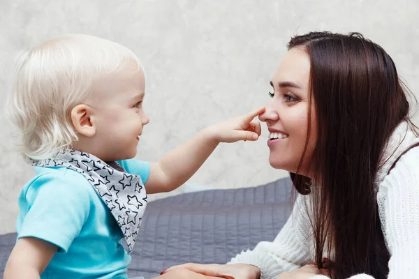 A young pretty mother with her son. Blond boy and woman are sitting on the couch and playing. Family at home in the morning. Happy family portrait