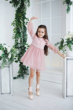 Pembe elbiseli bir genç uzun saçlı balerin yeşil dallar tarafından çerçeveli pointe yerinde duruyor