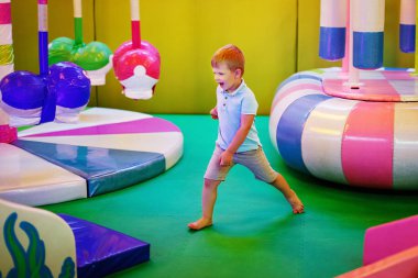 Sevimli küçük çocuk mavi tişört içinde kapalı çocuk oyun üzerinde oynuyor.