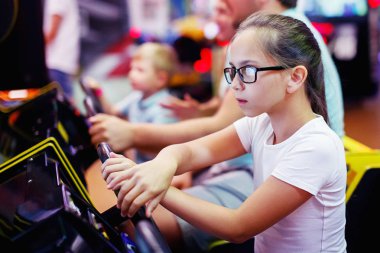 Aile Anne, Baba, gözlüklü genç kız ve küçük çocuk sürüş araba arcade oyun makinesi bir eğlence parkı. Seçici odak.