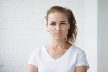 Genç kadın beyaz t-shirt beyaz bir arka plan üzerinde kamera ve pozlar bakar, uyuşuklar eğlenceli yüzler, şımartmanızı ve gülümsüyor.