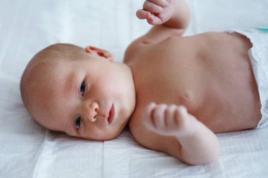 Yedi günlük eski bebek çıplak sırt üstü beyaz bir levha üzerinde yatıyor ve duygular gösterir. Bebeğin başını seçici odak. Çocuk doğrudan kameraya benziyor. Yakın çekim.