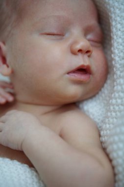 Yedi günlük eski bebek arkasında uyuyor. Çocuk bir battaniyeye sarılmış ve duygular uyku sırasında ifade eder. Yakın çekim.