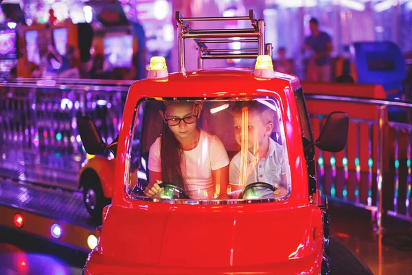 可爱的十几岁的女孩和小男孩骑在一个玩具汽车拱廊在一个游乐园游戏机的旋转木马 — 图库照片