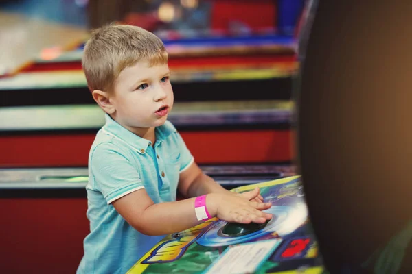 Cute boy in blue t-shirt plays arcade in game machine at an amusement park.