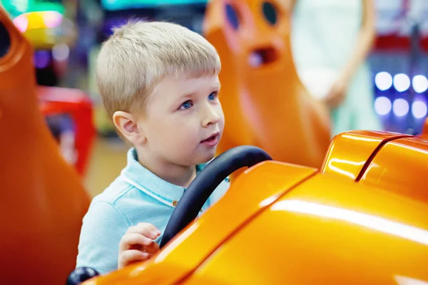 遊園地でゲーム機で運転して車アーケードかわいい金髪男の子 — ストック写真