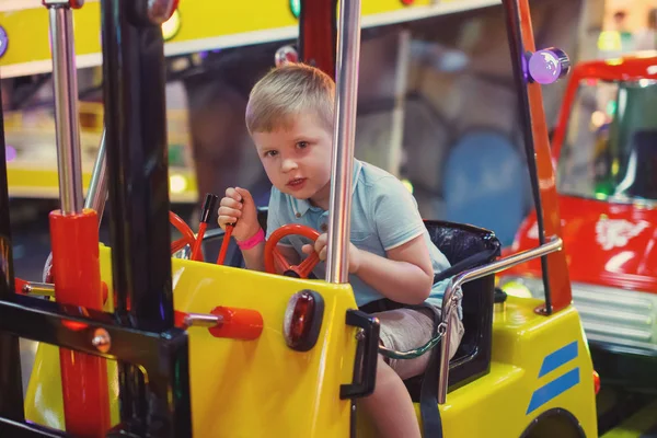 可爱的小男孩在蓝色 T恤骑在一个玩具车拱廊在游戏机在游乐园的旋转木马 — 图库照片