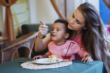 Pembe bir kazak ve uzun saç sit sokakta bir kafede bir masada beyaz annesiyle küçük karışık çocuk.