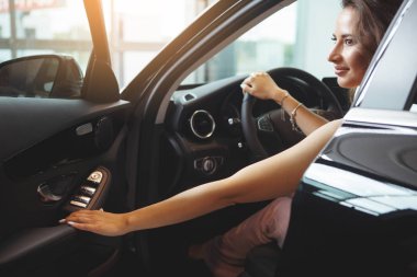 Uzun kıvırcık saçlı güzel güzel kız siyah bir arabada oturuyor. Sadece bir araba bayilik olarak al. Bir araç satın alma kavramı.