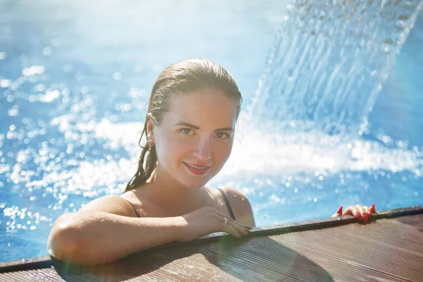 Young beautiful woman under a waterfall in a pool with clear blue water.