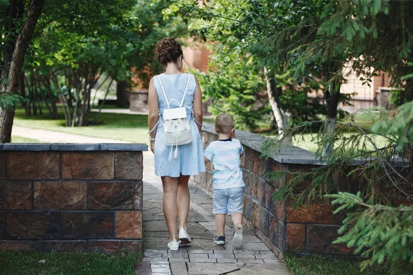 Young happy family: mother and blond boy walking on a stone pavement in the park. The concept of family well-being and a healthy lifestyle.