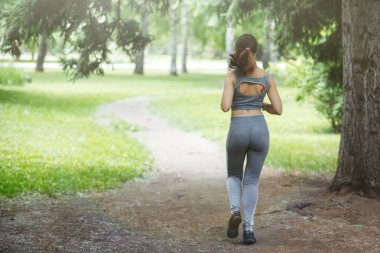 Genç kadın bir yeşil parkta bir yolda koşu. Arkadan görünüm.