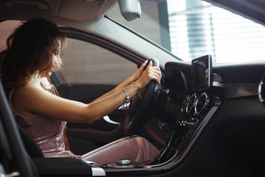 Uzun kıvırcık saçlı güzel güzel kız oturuyor ve direksiyon simidi siyah bir araba tutar. Sadece bir araba bayilik olarak al. Bir araç satın alma kavramı.