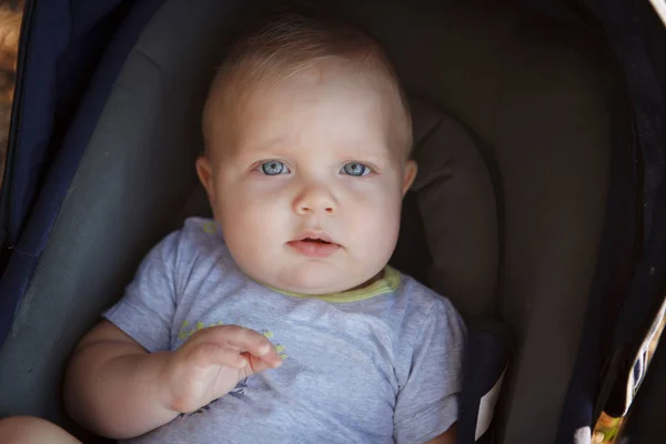 澄んだ瞳でカメラを見て暗い青色のベビーカーで金髪の赤ん坊 — ストック写真