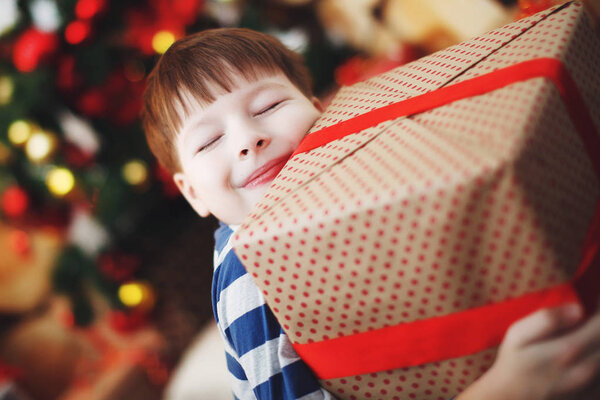 Boy in Christmas hats is sitting with gift boxes in his hands with the joy of a surprise.