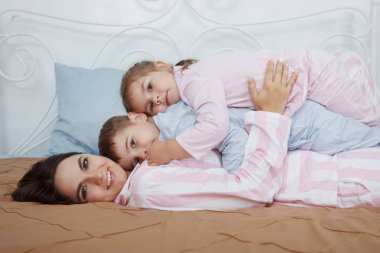 Genç şirin koyu saçlı kadın anne ve kızı pigtails ve oğluyla pembe ve mavi pijama yatağa yatak örtüsü ile yalan.