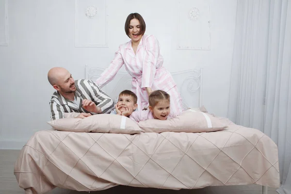 若いかなり枕やピンクの寝具が付いているベッドでパジャマ姿で遊ぶ息子と娘と女の母とハンサムなハゲ男の父 — ストック写真