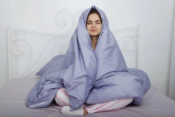 ピンクのパジャマで若い美しい女性がブルーの寝具とベッドの頭の上毛布で座っています — ストック写真