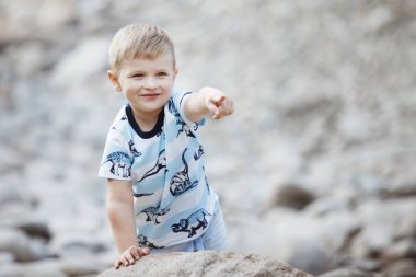 Sarışın oğlan mavi tişört içinde bir şehir parkı içinde gri taş olan oynuyor.