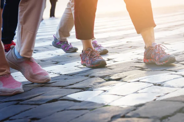Many diverse human legs are striding along the pavement of old gray stones. People walking on the sidewalk.