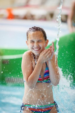 Genç güzel kız bir çizgili renkli mayo gülüyor, bir Aquapark bir şelale altında duruyor.