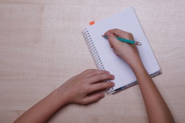 Çocuk ellerini masaya koy. Bir defter bir kalem ile çocuk yazıyor.