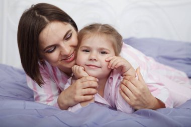 Genç güzel kadın anne kızıyla iki kuyruklu mavi yatak örtüsü ile yatakta birlikte oynamaktan.