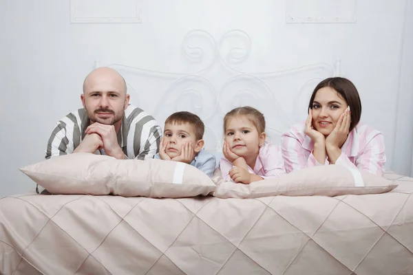 Young pretty woman mother and handsome bald man father with son and daughter in pajamas in bed with pillows and pink bedclothes.
