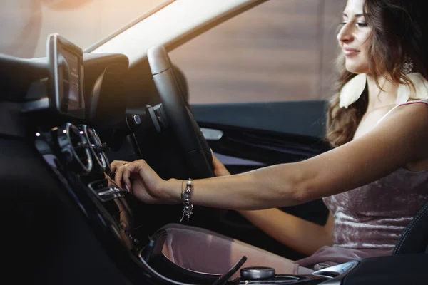 Nice beautiful girl with long curly hair is sitting in a black car. Just buy a car in the dealership. The concept of buying a vehicle.