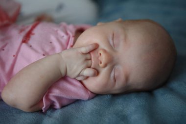 Küçük iki aylık şirin kız mavi battaniye var kapalı gözleri ile yatıyor ve elini ağzına tutar.