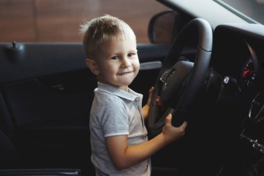 Komik küçük çocuk yeni bir otomobil kulübede oturuyor ve mutlu. Sadece bir araba satıcısı Center'da al. Bir araç satın alma kavramı.