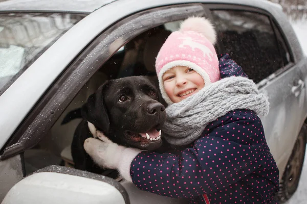 Dziewczyna i retweaver czarny Labrador w oknie samochodu są przytulanie w zimowym lesie. — Zdjęcie stockowe