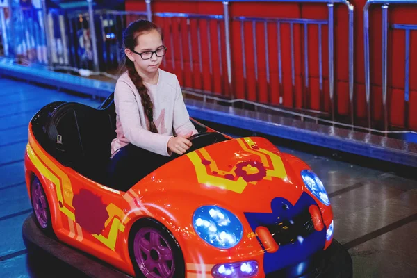 Ung söt flicka i glasögon med en tofsar som rider en leksak elbil. Joyfull helg. Nöjet att resa. — Stockfoto