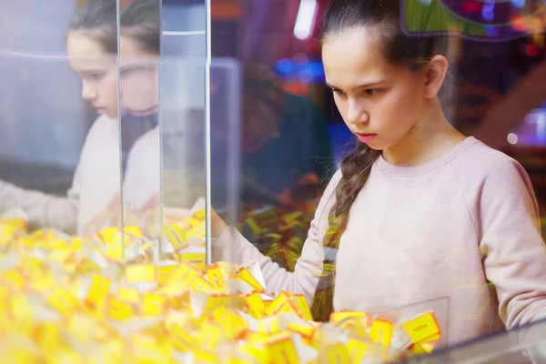 Молода красива дівчина з косичкою ретельно оглядає призи в ігровому автоматі. Радісні вихідні. Задоволення і удача в грі . — стокове фото