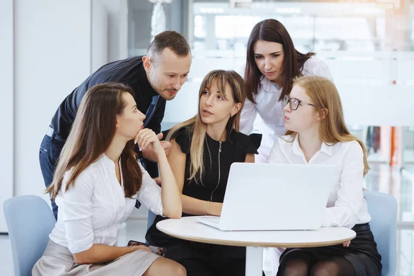 Team of office staff. Business woman and man sit and stand next to the table with a laptop and plan the concept of the corporation for the future. Teamwork. Gender equality.