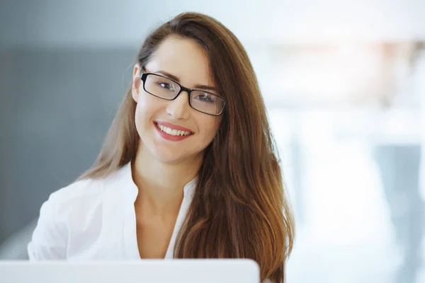 Business woman in a white blouse sitting at a table with a laptop in the office and smiling. Gender equality. Good deal. Favorable agreement. Female leadership.
