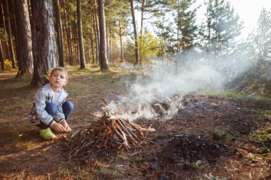 Ekose gömlekli çocuk sonbahar ormanda bir yangın yap.