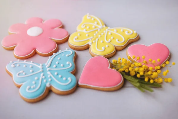 Colored gingerbread cookies in the shape of a heart, a butterfly and a flower with a sprig of yellow mimosa on a gray wooden background. For decoration, web design. Overall plan.