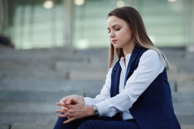 Mavi bir takım elbise genç güzel kadın bir gri taş merdiven parlayan ışıklar bir arka plan üzerinde oturuyor.