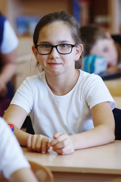 可爱的少女眼镜坐在她的办公桌在学校 并阐述教师的任务 — 图库照片