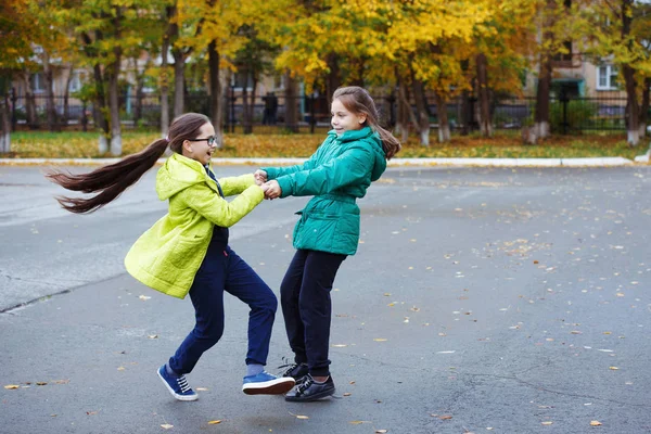两个穿着黄色和绿色夹克的年轻美女青少年玩耍 玩得很开心 在秋场跳舞 为摄影师摆姿势 — 图库照片