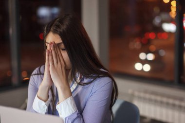 Masada laptop ile çalışma gece ofiste iş kadını. Pencerenin dışında çeşitli renklerde ışık yanıyor. Son Tarih, fazla mesai.