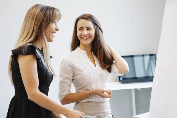 Teams of office staff. Two Business women stand talking near the tablet board. Teamwork. Gender equality.