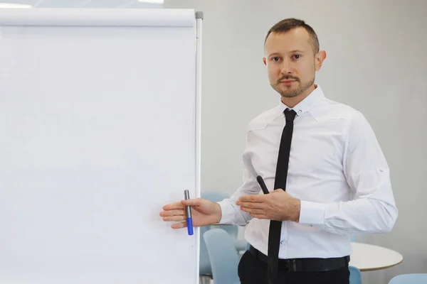 Teamwork of office staff. Businessman coach in a white shirt and tie, standing near the flipchart, explains the schedule of tasks for the future. Business training. Personal growth.