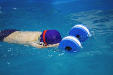 Üç-yıl-yaşlı oğlan mavi bir kap ve yüzme gözlük bir köpük oyuncak kullanarak bir havuzda yüzüyor. Dalış. Sağlıklı bir yaşam tarzı. Aquatherapy. Yüzme rehabilitasyon.