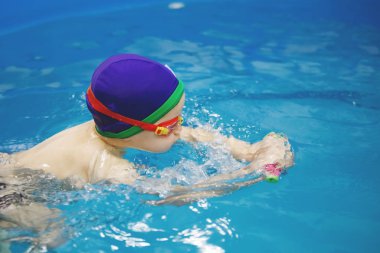 Üç-yıl-yaşlı oğlan mavi bir kap ve yüzme gözlüğü köpük stick kullanarak bir havuzda yüzüyor. Dalış. Sağlıklı bir yaşam tarzı. Aquatherapy. Yüzme rehabilitasyon.